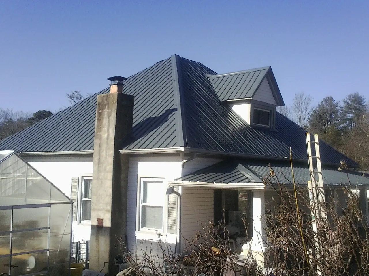 Dark blue standing seam metal roof on a white farmhouse with dormer — Slate & Tile Roof Repair by Roofing Brothers in Bernalillo
