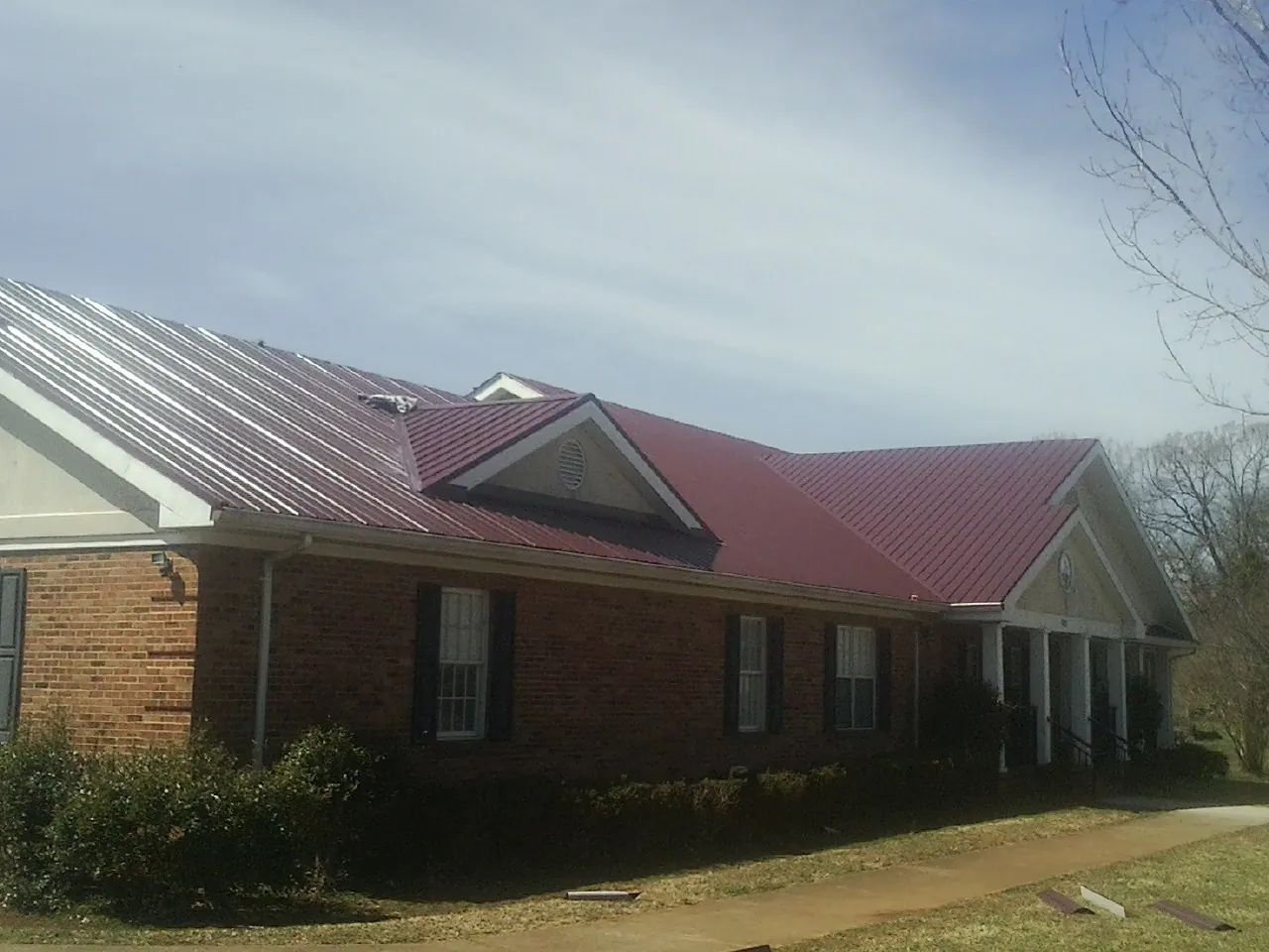 Red metal roof with gabled entries on a long brick building, from a Hail Damage Roof Repair job in Bernalillo