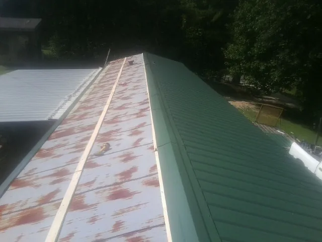 Old rusted panels beside newly installed green metal roofing — Wind Damage Roof Repair by Roofing Brothers in Bernalillo